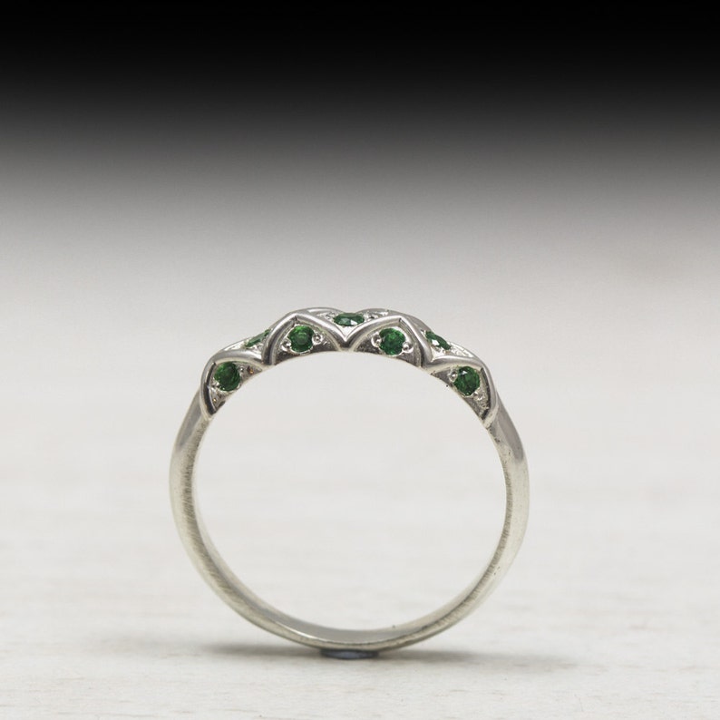 Puede incluir: Un anillo de banda de plata con una fila de peque&ntilde;as piedras preciosas verdes engastadas en un dise&ntilde;o delicado.