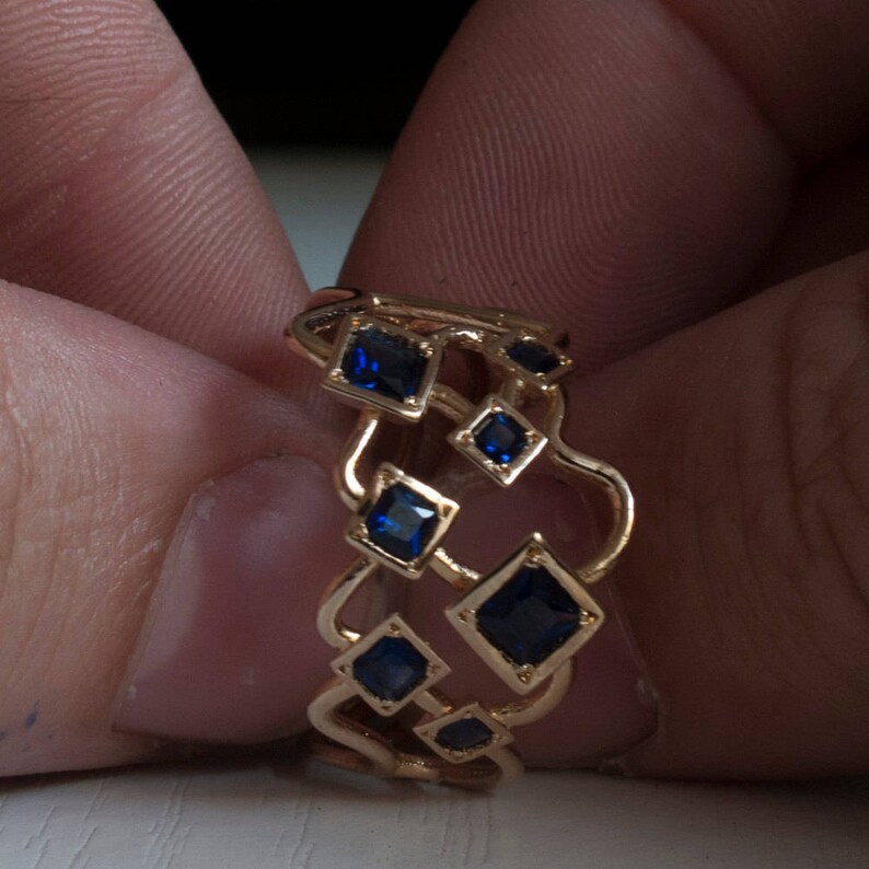 May include: A gold ring with a geometric design featuring multiple blue square-shaped gemstones.