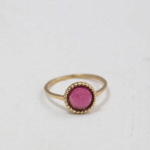 Puede incluir: Un anillo de oro con una piedra preciosa rosa engastada en un engaste de cuentas.