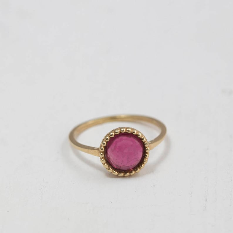 Puede incluir: Un anillo de oro con una piedra preciosa rosa engastada en un engaste de cuentas.
