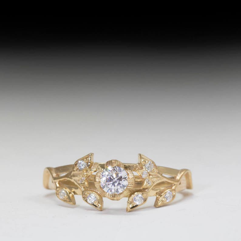 May include: A gold ring with a delicate floral design featuring a round, clear center stone and smaller accent stones. The ring is set on a white background.