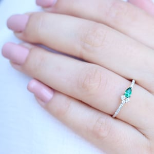 May include: A delicate silver ring with a pear-shaped emerald gemstone and smaller diamonds set in a pave setting.