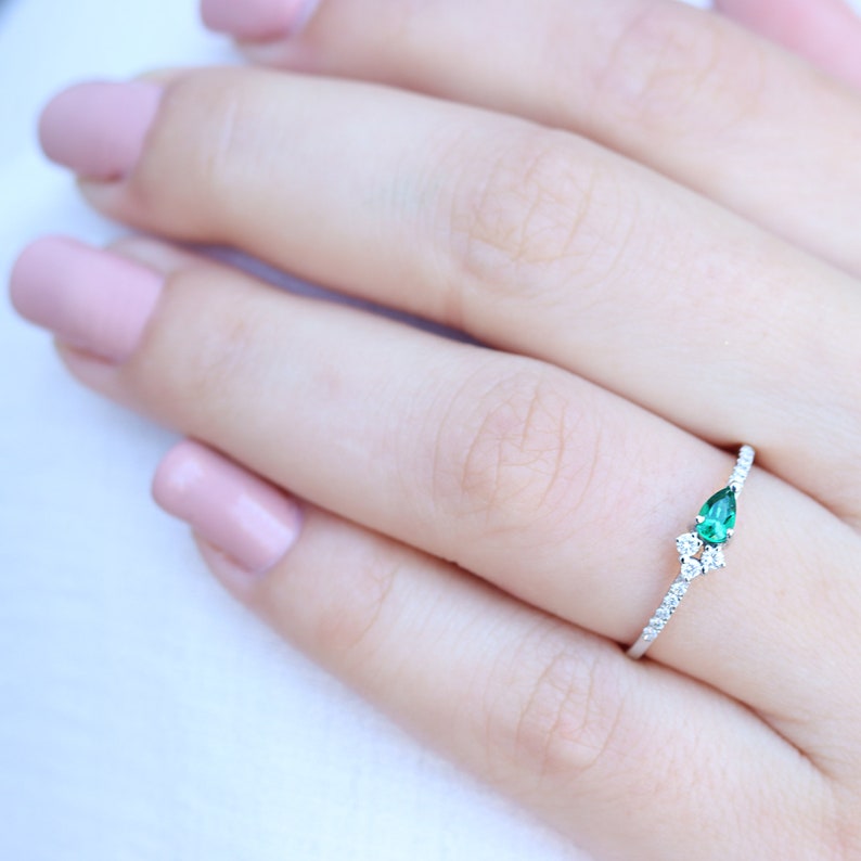 May include: A delicate silver ring with a pear-shaped emerald gemstone and smaller diamonds set in a pave setting.