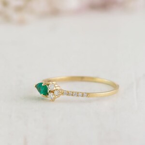 May include: A delicate gold ring with a pear-shaped emerald gemstone and a row of small diamonds.