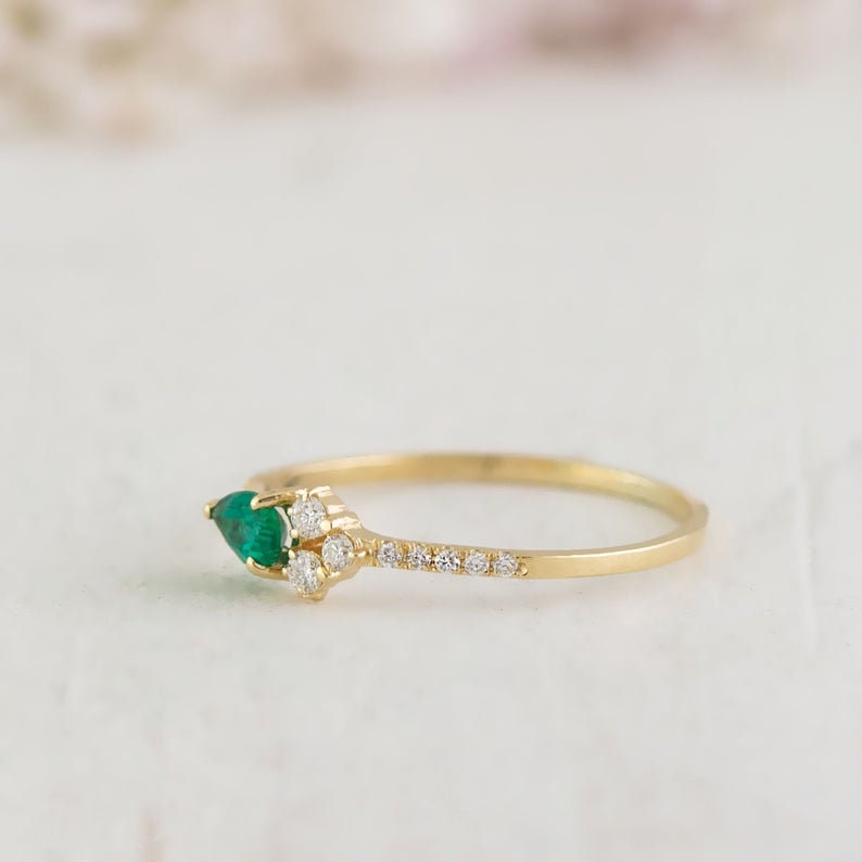May include: A delicate gold ring with a pear-shaped emerald gemstone and a row of small diamonds.