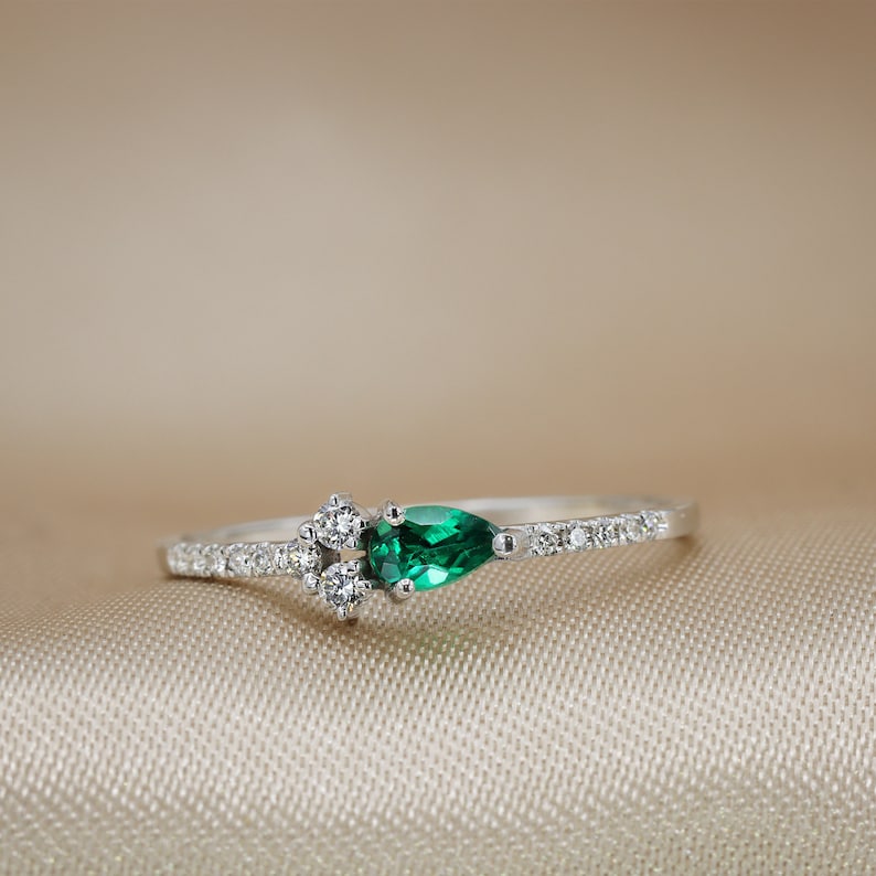 May include: A delicate silver ring with a pear-shaped emerald green gemstone and smaller diamonds set in the band.