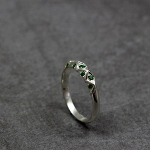Puede incluir: Un anillo de banda de plata con un dise&ntilde;o geom&eacute;trico con piedras preciosas verdes.