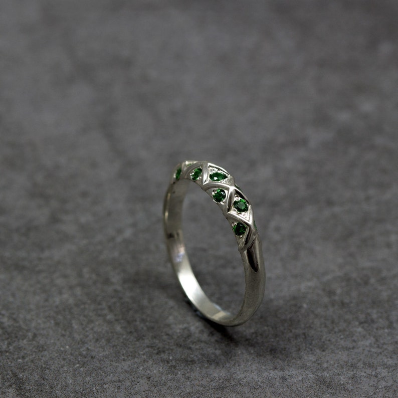 Puede incluir: Un anillo de banda de plata con un dise&ntilde;o geom&eacute;trico con piedras preciosas verdes.