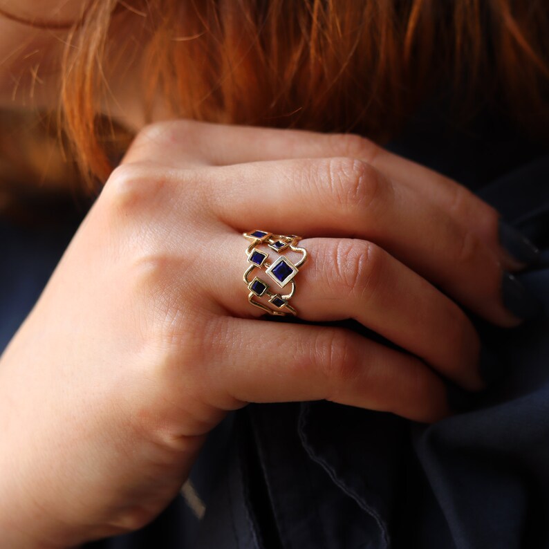 May include: Gold ring with a geometric design featuring multiple blue square-shaped stones.