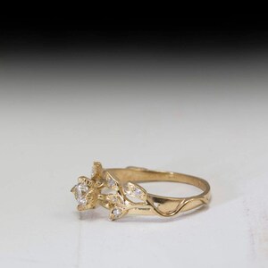 May include: A gold ring with a single round diamond set in a floral design. The band is thin and delicate, with a vine-like pattern.