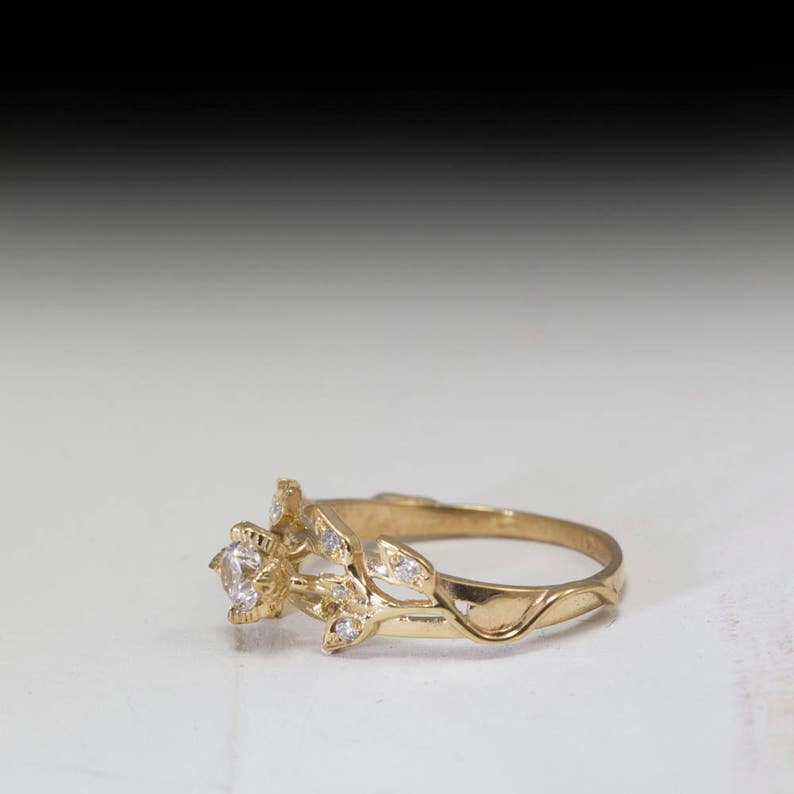 May include: A gold ring with a single round diamond set in a floral design. The band is thin and delicate, with a vine-like pattern.