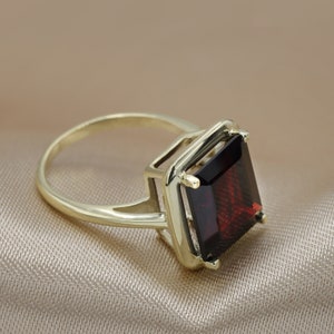 Puede incluir: Un anillo de oro con una piedra preciosa grande de color rojo oscuro de forma cuadrada.