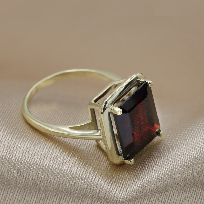 Puede incluir: Un anillo de oro con una piedra preciosa grande de color rojo oscuro de forma cuadrada.