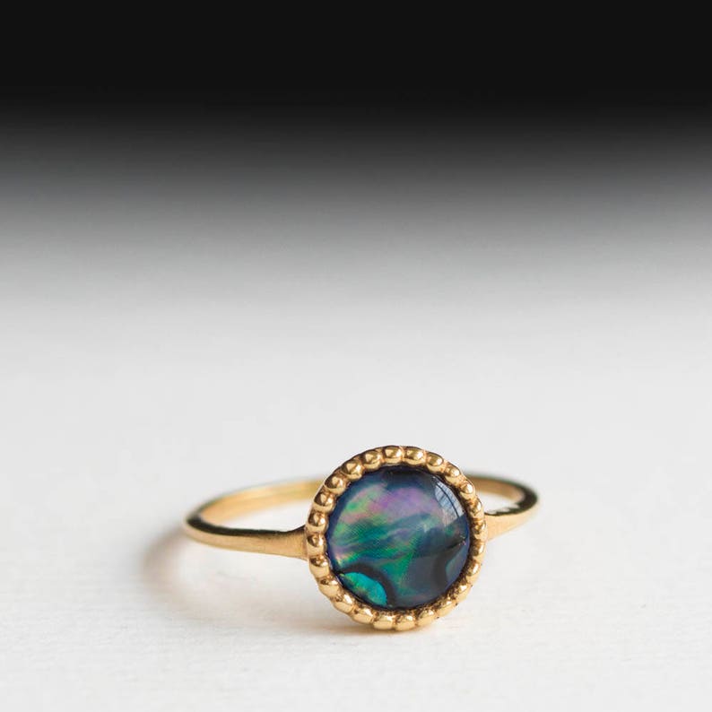 May include: A gold ring with a round, iridescent blue and green abalone shell stone.