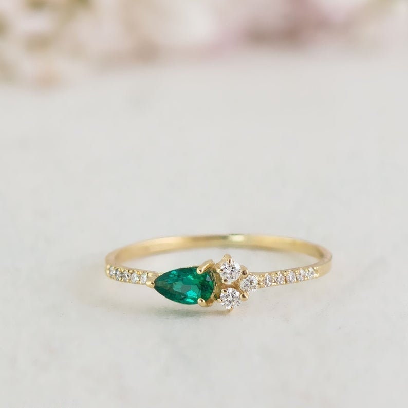 May include: A delicate gold ring with a pear-shaped emerald gemstone and smaller round diamonds set in a pave band.