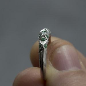 Puede incluir: Un anillo de plata con un dise&ntilde;o de cruz y piedras preciosas verdes.