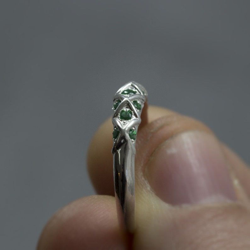Puede incluir: Un anillo de plata con un dise&ntilde;o de cruz y piedras preciosas verdes.