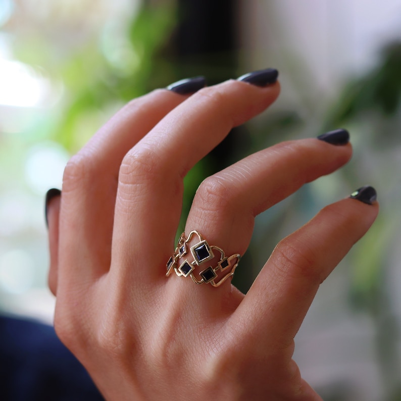 May include: A gold ring with a geometric design featuring black square stones.