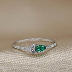May include: A delicate silver ring with a pear-shaped emerald green gemstone and a cluster of smaller clear gemstones.