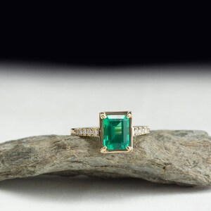 May include: A gold ring with a large emerald green gemstone and a band of small diamonds.