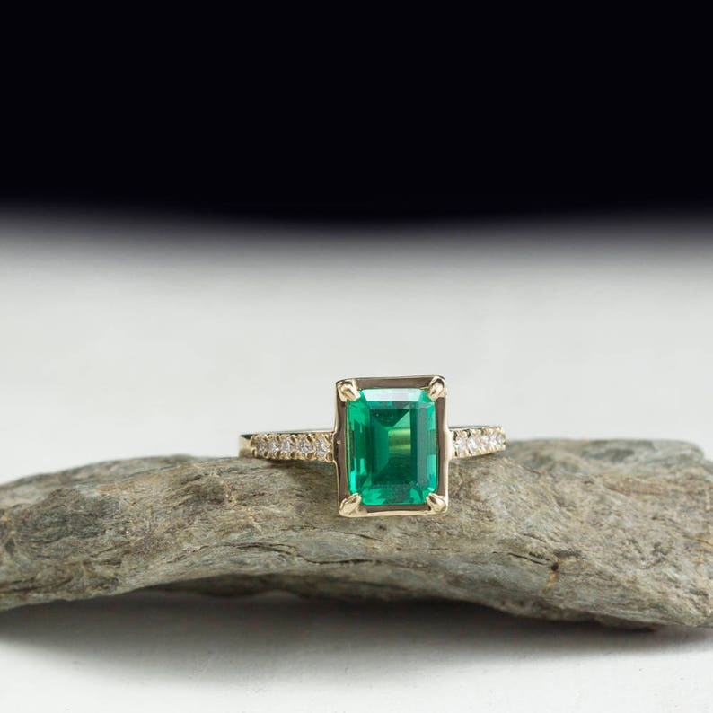 May include: A gold ring with a large emerald green gemstone and a band of small diamonds.