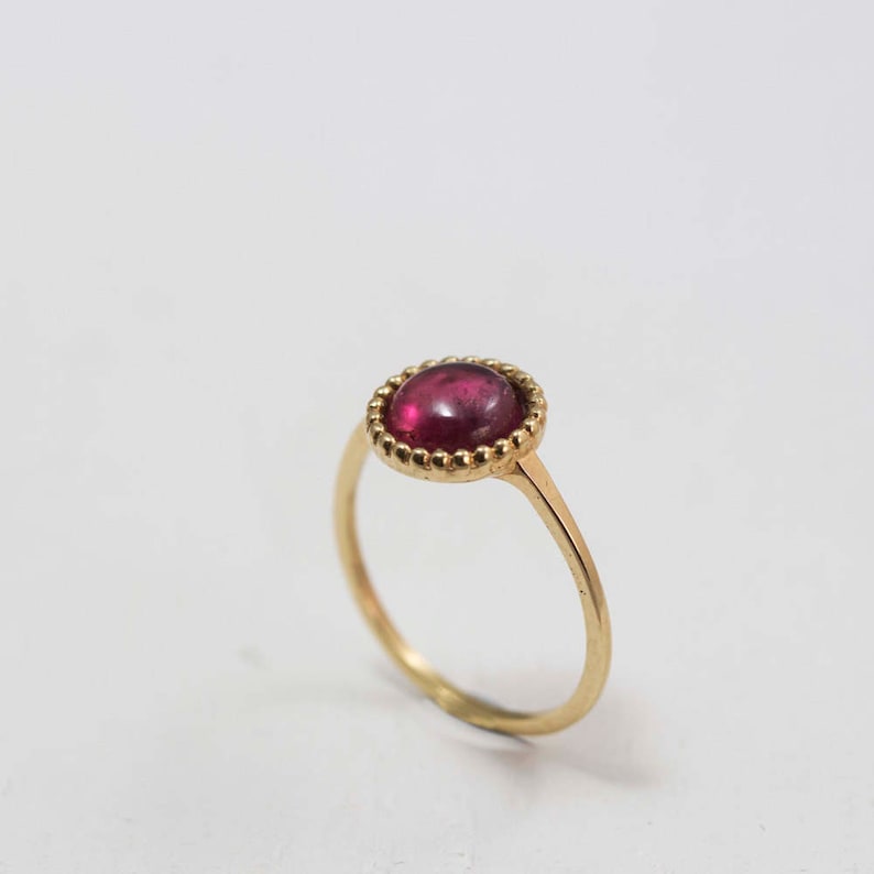 Puede incluir: Un anillo de oro con una piedra preciosa roja engastada en un engaste de cuentas.