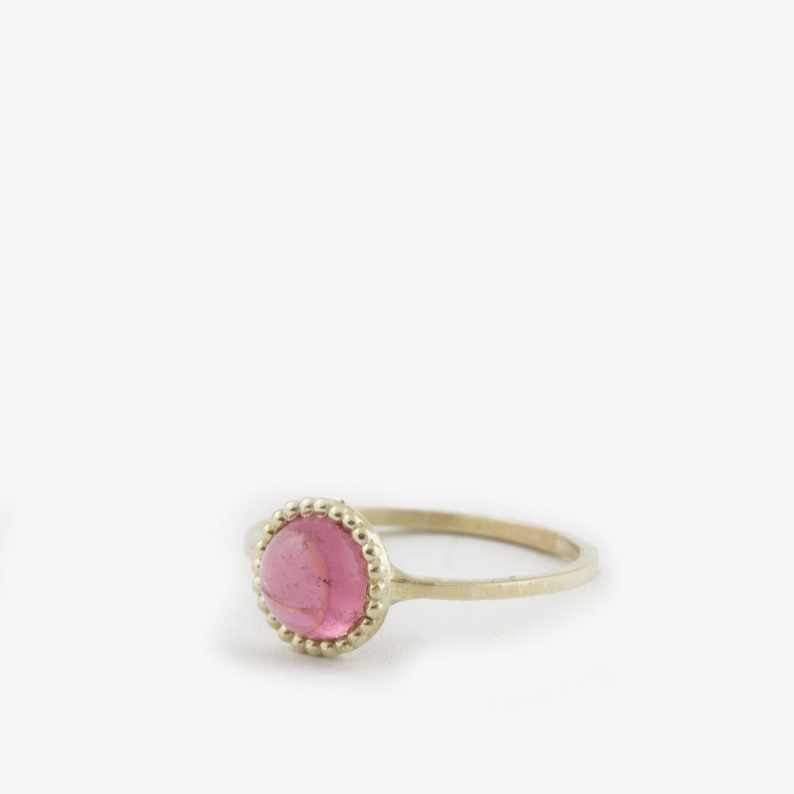 Puede incluir: Un delicado anillo de oro con una piedra preciosa rosa engastada en un engaste de cuentas.