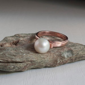 May include: A rose gold ring with a single white pearl set in the center.