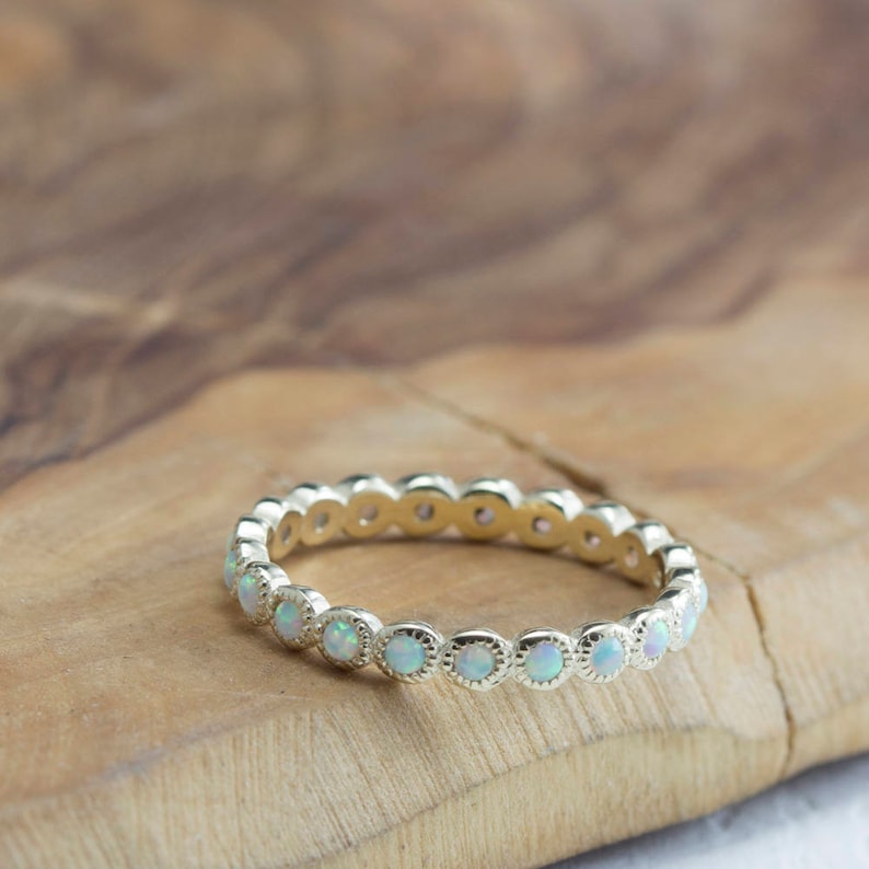 Puede incluir: Un delicado anillo de banda de oro con una fila de peque&ntilde;as piedras redondas de &oacute;palo blanco.