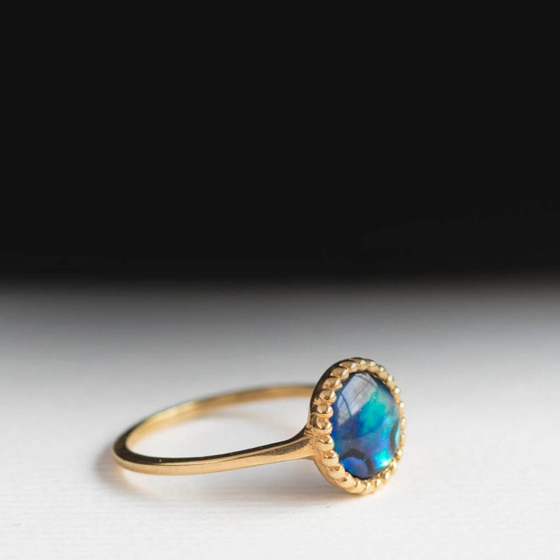 May include: A gold ring with a blue and green abalone shell set in a beaded bezel.