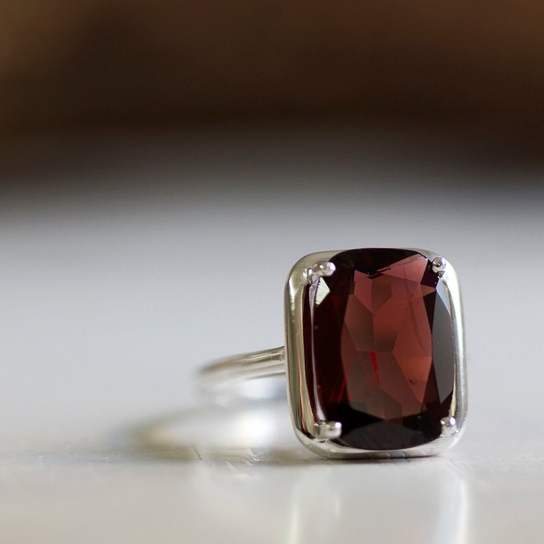 Puede incluir: Un anillo de plata con una gran piedra preciosa rectangular de color rojo oscuro.