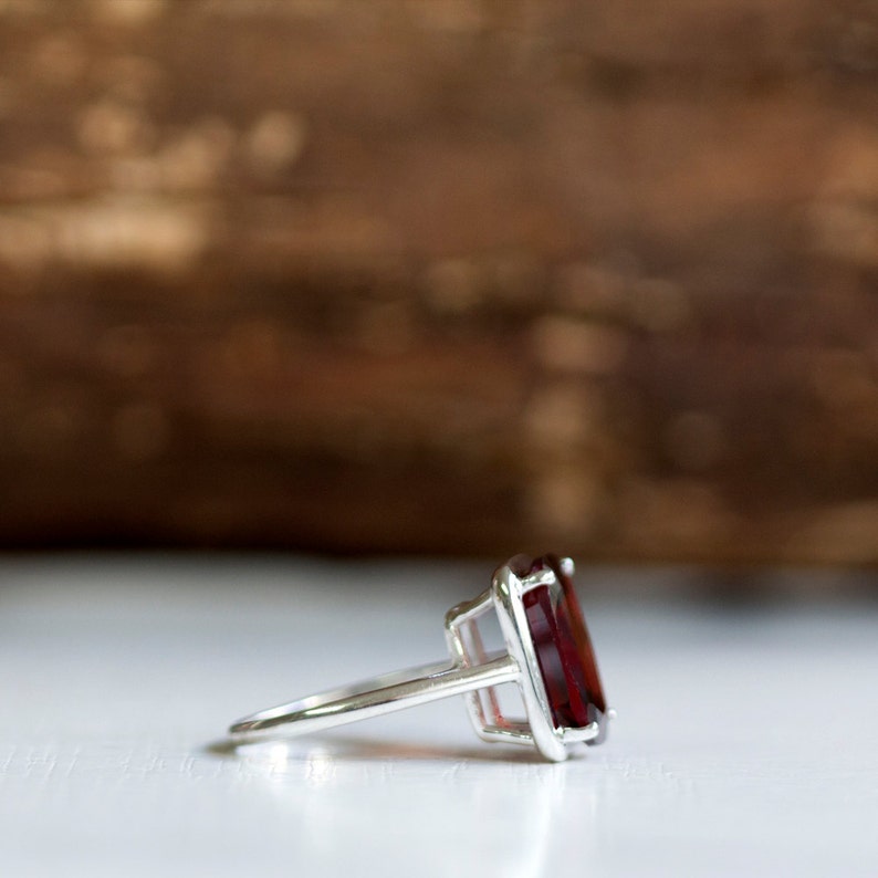 Puede incluir: Un anillo de plata con una gran piedra preciosa de color rojo oscuro engastada en un engaste cuadrado.