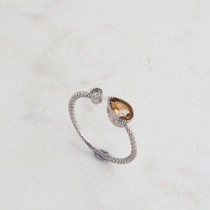 May include: A silver ring with a pear-shaped topaz gemstone and a smaller round clear stone.