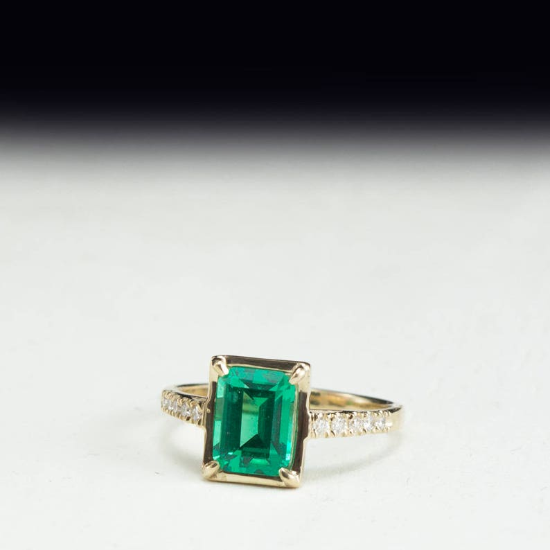 May include: A gold ring with a large emerald green gemstone and a band of small diamonds.