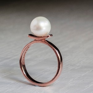 May include: A rose gold ring with a single white pearl set on top. The ring has a simple, modern design.