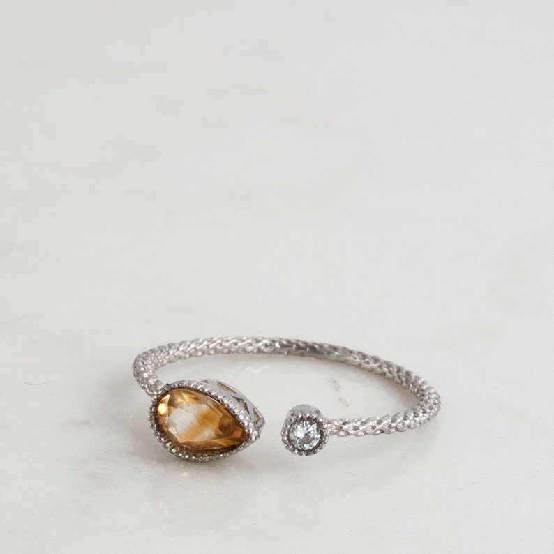 May include: A silver ring with a teardrop-shaped topaz gemstone and a smaller round clear gemstone.