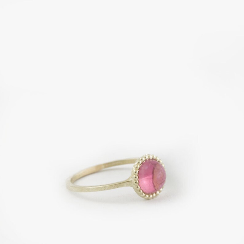 Puede incluir: Un delicado anillo de oro con una piedra preciosa rosa engastada en un engaste de cuentas.