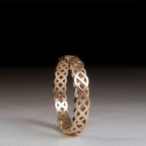 May include: A gold-colored ring with a delicate, intricate design of interwoven loops. The ring is made of metal and has a polished finish.