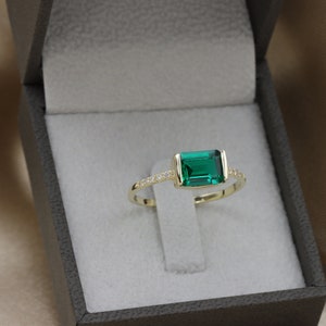 May include: A gold ring with a large emerald green gemstone and a row of small clear gemstones around the band.