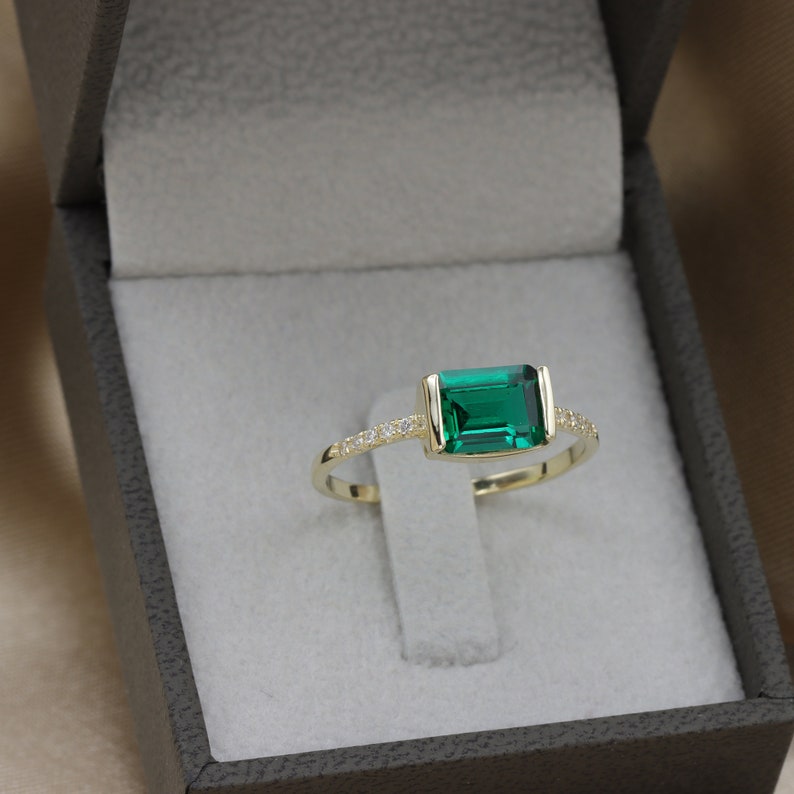 May include: A gold ring with a large emerald green gemstone and a row of small clear gemstones around the band.