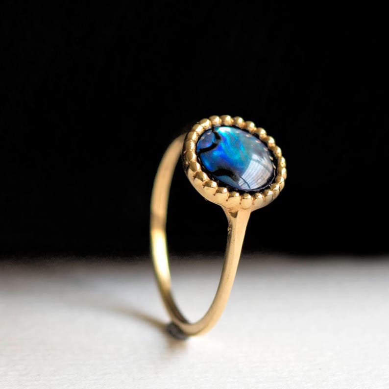 May include: A gold ring with a blue and green abalone shell set in a beaded bezel.