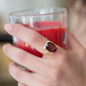 Puede incluir: Un anillo de oro con una piedra preciosa rectangular grande de color rojo oscuro.