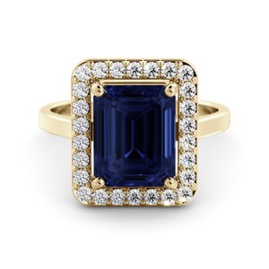 May include: A gold ring featuring a large, rectangular, deep blue gemstone surrounded by a halo of smaller, clear gemstones. The ring's band is a simple, polished gold. The setting is a classic, elegant design.