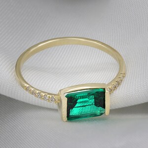 May include: A gold ring with a green emerald gemstone and a row of small diamonds around the band.