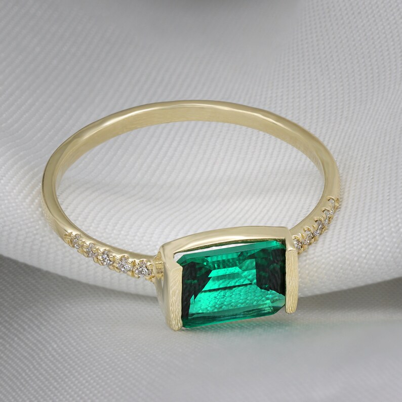 May include: A gold ring with a green emerald gemstone and a row of small diamonds around the band.