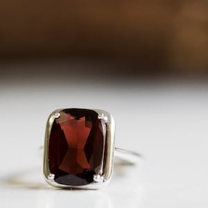 Puede incluir: Un anillo de plata con una piedra rectangular de color rojo oscuro grande.