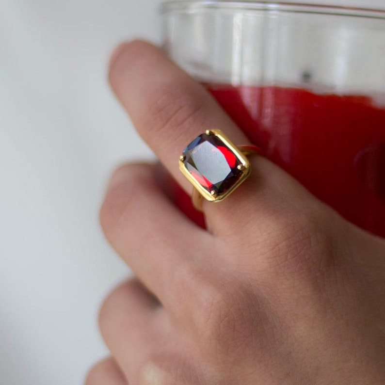 Puede incluir: Un anillo de oro con una piedra rectangular de color rojo oscuro grande.