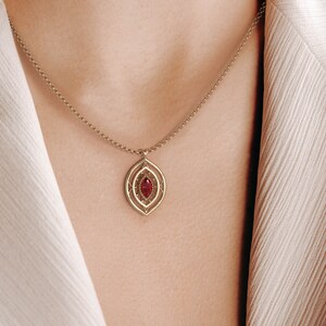 May include: A gold necklace with a red gemstone pendant. The pendant is a delicate, intricate design with a marquise-shaped stone.