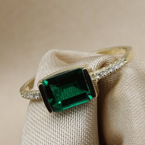 May include: A gold ring with a large emerald green gemstone and a row of small diamonds around the band.