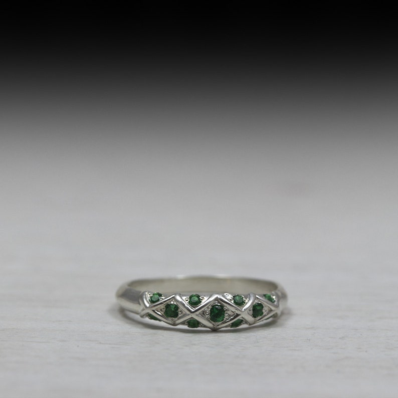 Puede incluir: Un anillo de banda de plata con un dise&ntilde;o delicado que presenta una fila de peque&ntilde;as piedras preciosas verdes.